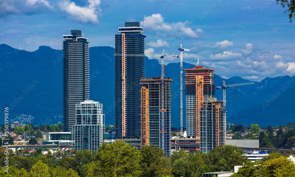 Construction of New Residential District  in the city of Burnaby, high-rise buildings under construction and construction cranes  against the backdrop of a mountain ridge
