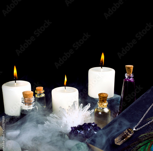 Magic potions  crystals  book  stones  peacock feather  and candles with smoke on a black background.