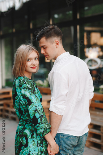 Love story, a man and a blonde girl. Loving couple sitting hugging, kissing, looking at each other, smiling and laughing, on a European city street in the summer. In casual wear. 