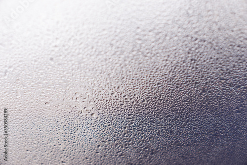 Closeup photo of a foggy window glass in drops of water.