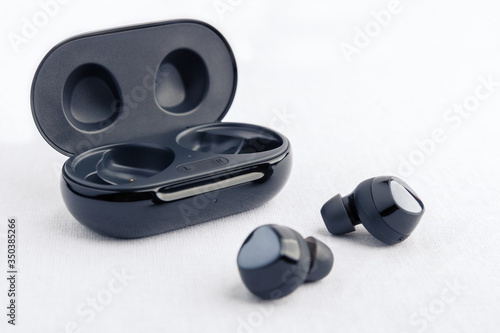 Earbud headphones side profile - displayed in front of opened black wireless earbud charging case