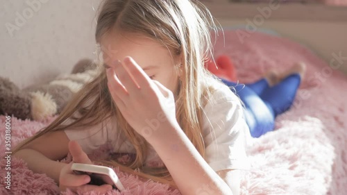 Girl plays the phone lying on the bed in her room.