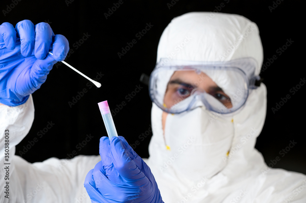 Medical healthcare technologist holding COVID-19 swab collection kit, wearing white PPE protective suit mask gloves, test tube for taking patient specimen sample . Medical healthcare technologist holding COVID-19 swab collection kit, wearing white PPE protective suit mask gloves, test tube for taking patient specimen sample .