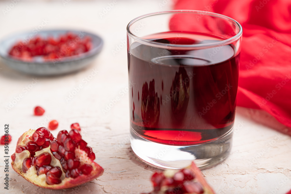 Glass of pomegranate juice on a white concrete background. Side view, selective focus Glass of pomegranate juice on a white concrete background. Side view, selective focus