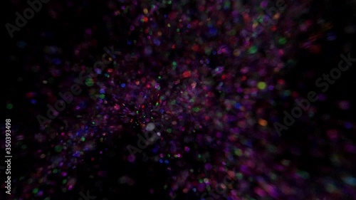 Multi-colored glitter bomb exploding and glitter falling from the sky from black background