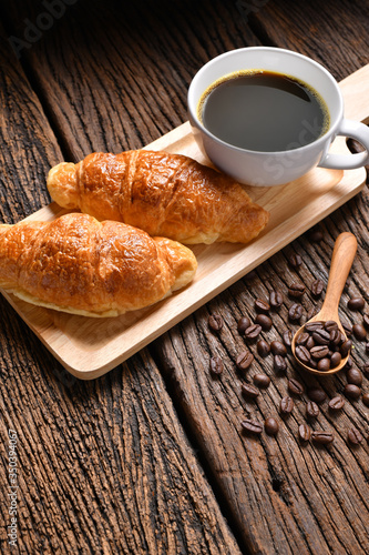 A cup of coffee with coffee beans and croissant on wooden table