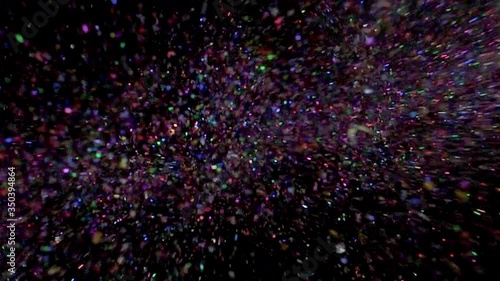 Multi-colored glitter bomb exploding and glitter falling from the sky from black background