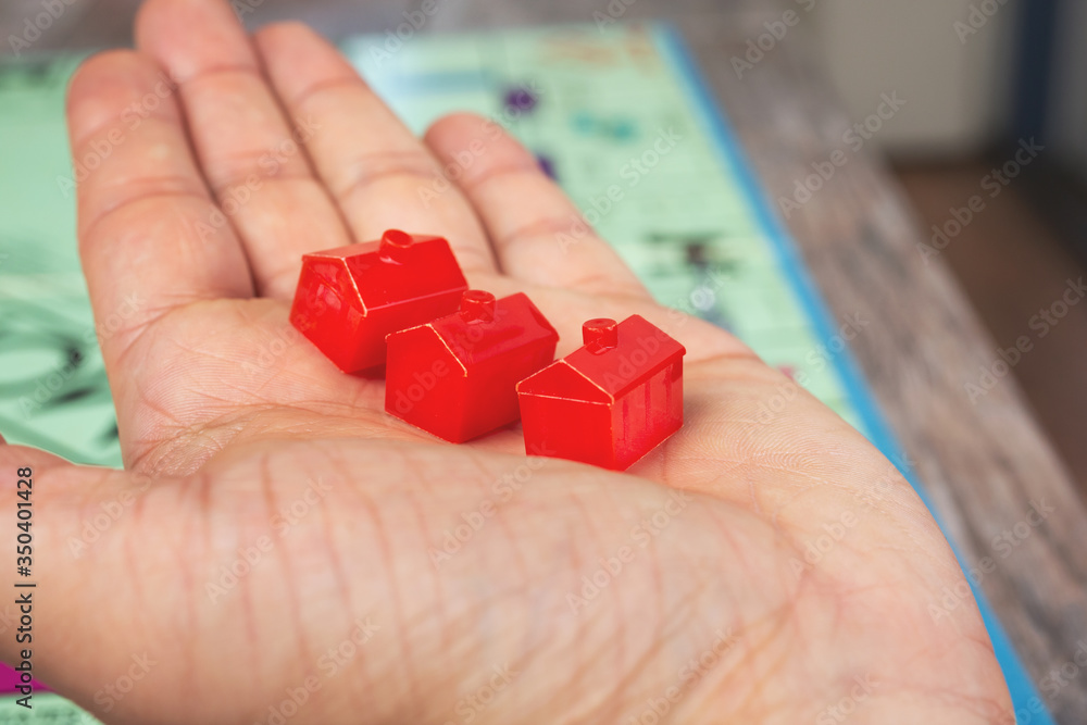 A view of a hand holding several red hotel markers, over a fun popular money and finance board game.