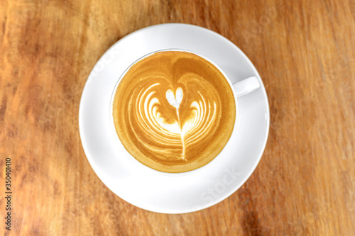 Hot latte coffee in white ceramic cup and saucer placed on wood table (Top view)