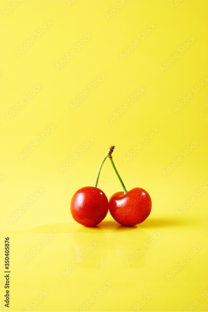Two red cherries against yellow background