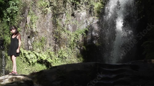 Person standing in front of Amazing Huge Waterfall in New Zealand, woman watching Falling water in nature hitting water surface slow motion, Lush green leafes is moving from the wind, Kaiate Falls photo