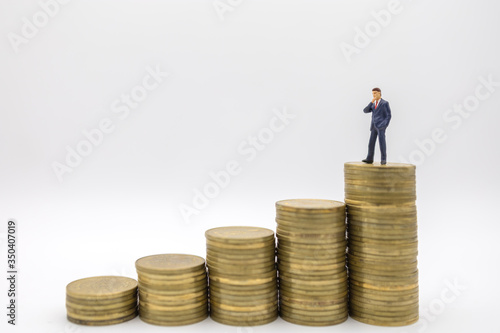 Business, Money Investment and Planning Concept. Close up of businessman miniature people figure standing on top of stack of gold coins on white background with copy sapce.