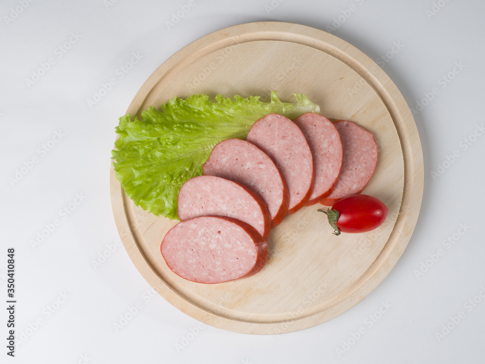Raw smoked sausage, cut into slices on a board. Near leaf lettuce and tomato Raw smoked sausage, cut into slices on a board. Near leaf lettuce and tomato