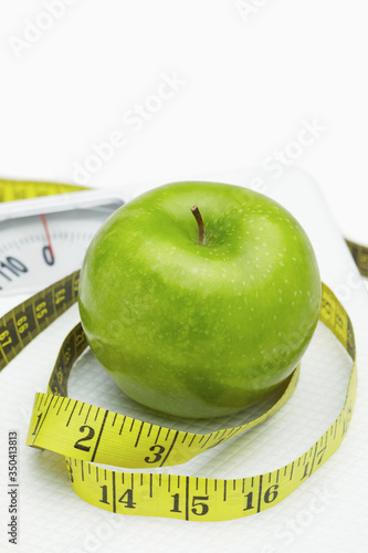 Measuring tape wound around a green apple on a weighing scale