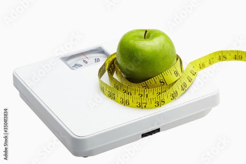 Measuring tape wound around a green apple on a weighing scale