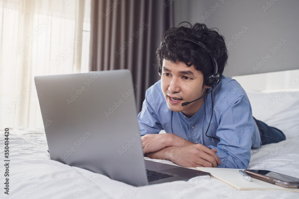 business man wear headset video conference calling on laptop computer on bed, work from home concept business man wear headset video conference calling on laptop computer on bed, work from home concept