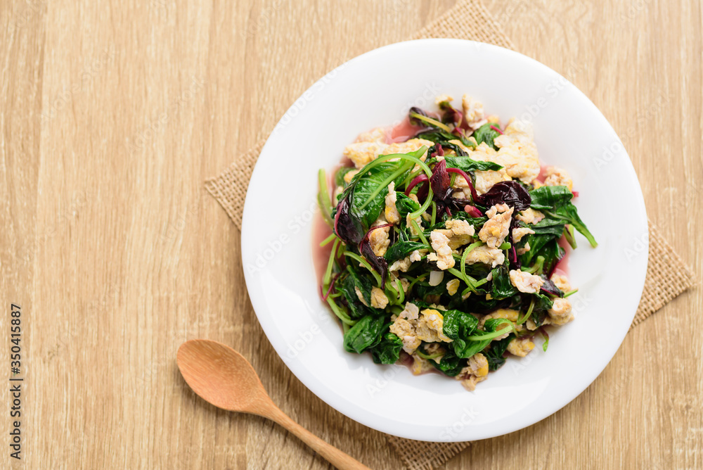 Stir fried Thai spinach with egg on white dish and spoon on wooden background, Healthy Thai food, Top view Stir fried Thai spinach with egg on white dish and spoon on wooden background, Healthy Thai food, Top view