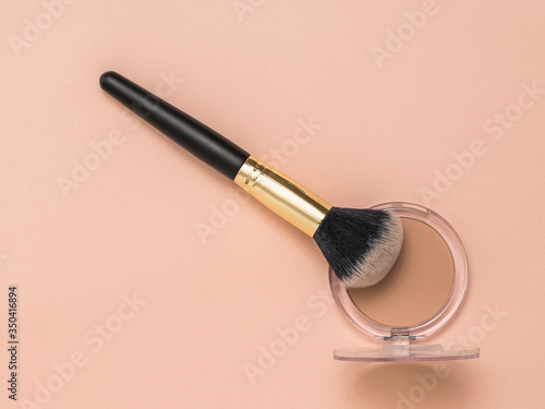 A makeup brush and a jar of powder on a pastel background.