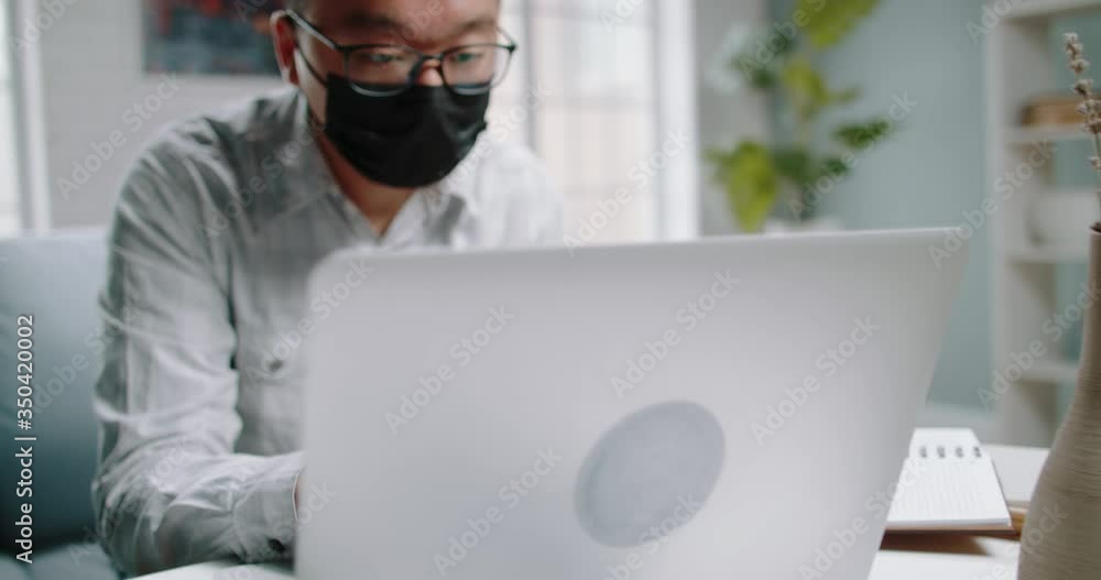 Young male chinese university student sheltering from viruses and infections at home, working at his laptop on unfinished project. Man wearing a mask to protect himself from disease 4k footage Young male chinese university student sheltering from viruses and infections at home, working at his laptop on unfinished project. Man wearing a mask to protect himself from disease 4k footage