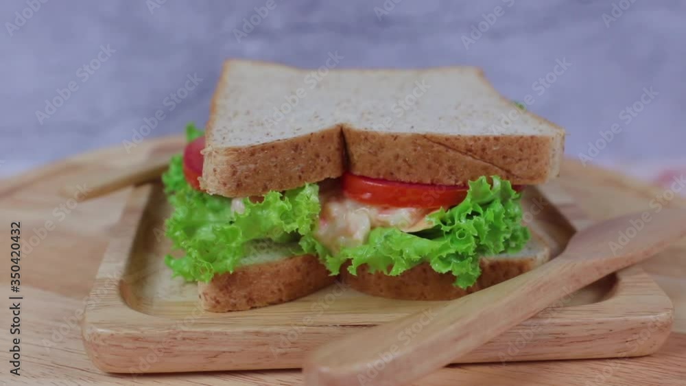 Homemade sandwich with toasted bread slices, Mayonnaise, tomato, salad leafs, carrots , mozzarella cheese on square wooden plate with wooden fork on the grate , on a Rotating on a round wooden plate. Homemade sandwich with toasted bread slices, Mayonnaise, tomato, salad leafs, carrots , mozzarella cheese on square wooden plate with wooden fork on the grate , on a Rotating on a round wooden plate.