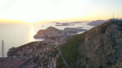Aerial view of Dubrovnik old town at the foot of mountain near Adriatic sea at sunset, Croatia. Forest on mountain. Orange roof tops of historic centre. Small islands archipelago in the sea.