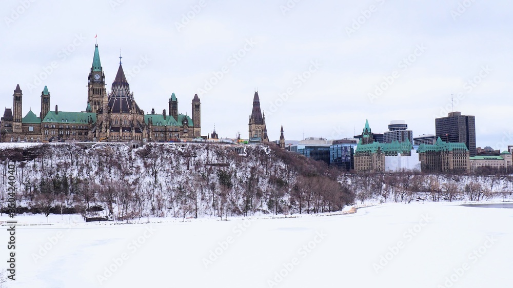 Obraz premium The Parliament Building on Canada stands tall on Parliament Hill on a cold winter day, with the Ottawa River still frozen from the dog days of winter. 