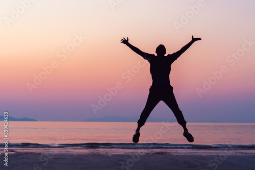 Fototapeta Naklejka Na Ścianę i Meble -  Silhouette man rise hands up and jump to sky freedom concept with sunset sky and summer beach season.