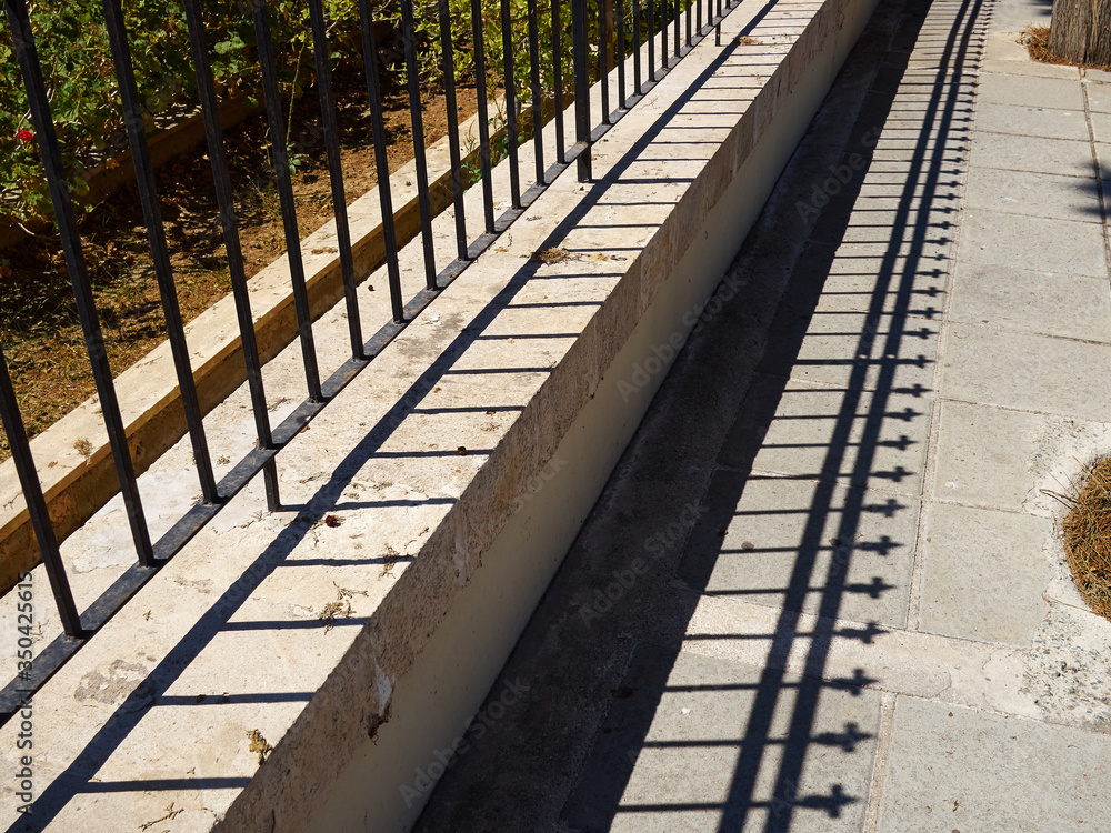 Iron fence and shade of it on a sidewalk Iron fence and shade of it on a sidewalk