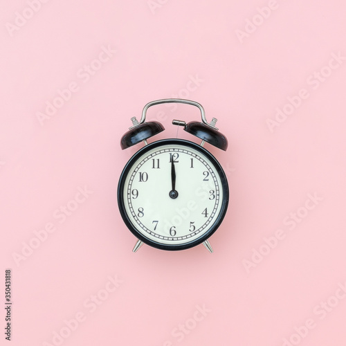 Black alarm clock in center on pink background, closeup. Minimal style Copy space Top view Template for your text, design