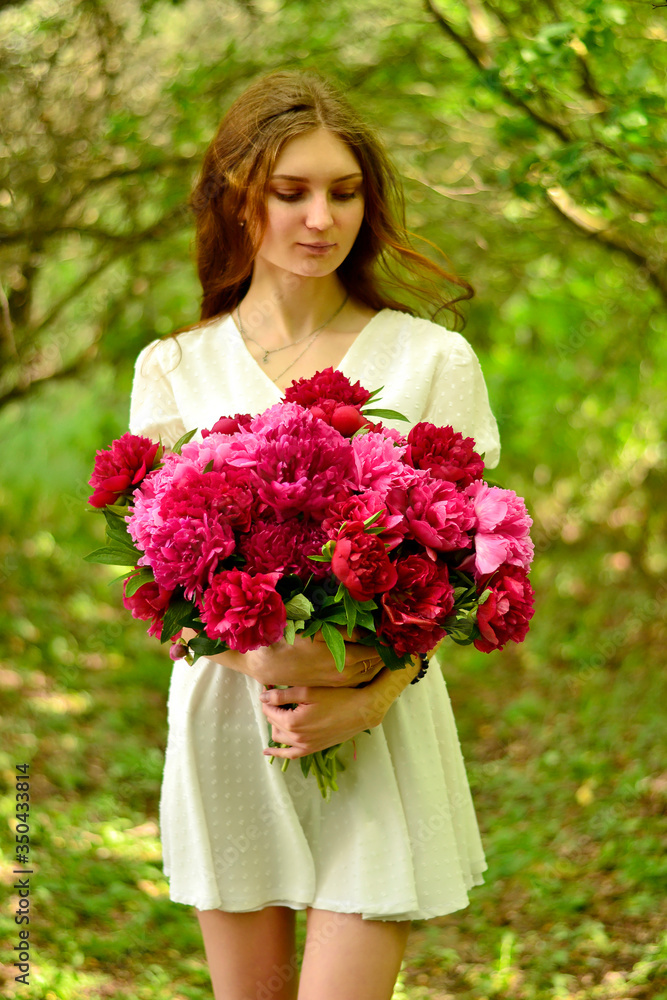 Slender brown-haired woman in a white dress with peonies in her hands