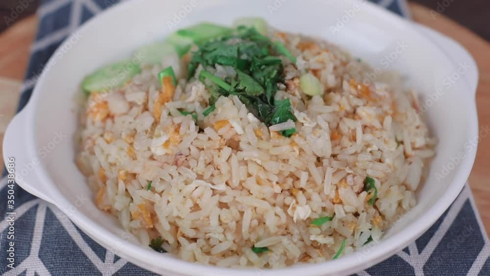 Fried rice with crab meat and onion, garlic, cucumber , egg in a white plate , rotating on a wooden plate Fried rice with crab meat and onion, garlic, cucumber , egg in a white plate , rotating on a wooden plate