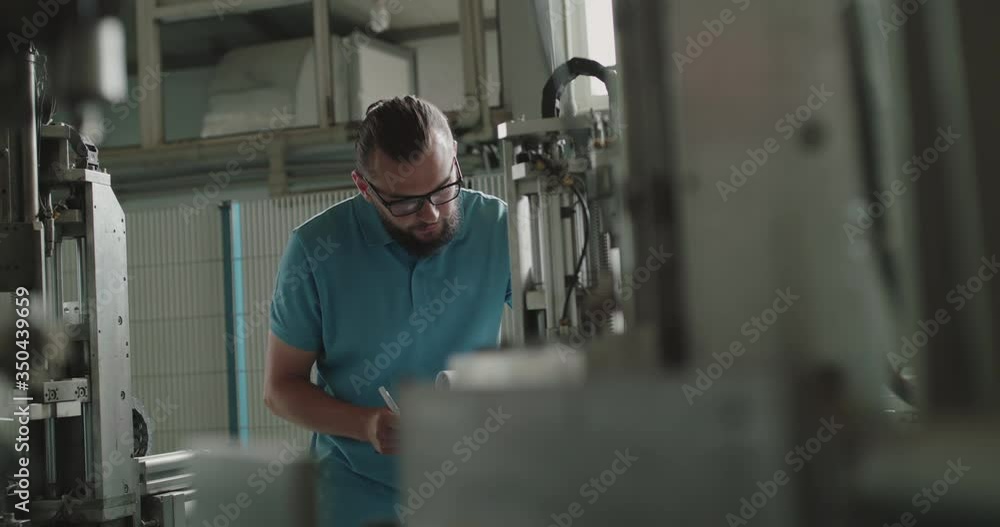 The engineer in glasses with notebook examining a serviceability of machine The engineer in glasses with notebook examining a serviceability of machine