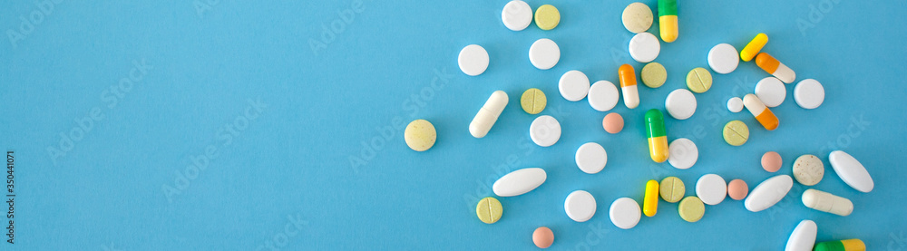 Colorful pills and capsules on blue background. prevention of coronavirus. Web banner on site with empty space for text on the left side. Isolated. Medical preparations close up Colorful pills and capsules on blue background. prevention of coronavirus. Web banner on site with empty space for text on the left side. Isolated. Medical preparations close up