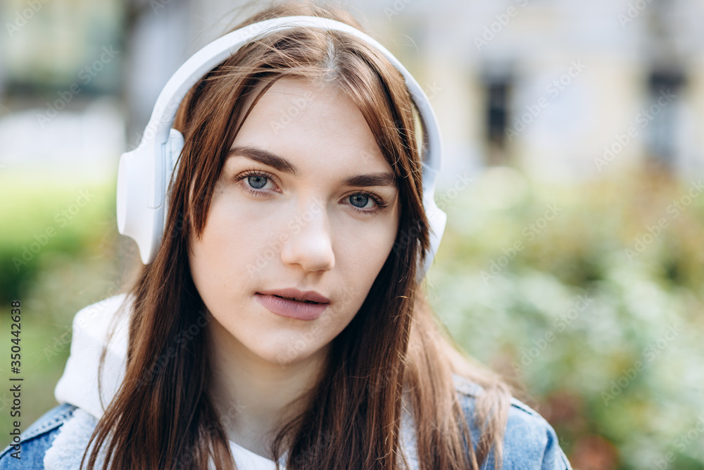 A serious girl in white headphones looks straight into the camera