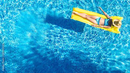 Girl relaxing in swimming pool, child swims on inflatable mattress and has fun in water on family vacation, tropical holiday resort, aerial drone view from above 