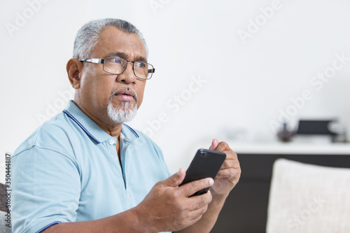 Senior man is thinking while holding a smartphone