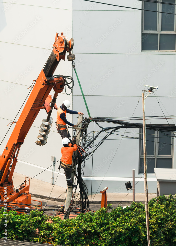 Electricians are climbing on electric poles with orange color crane to install and repair power lines.