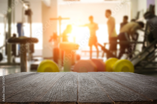 Empty wooden desk space over  blur fitness gym background. For product display montage. Business presentation.