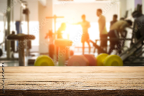 Empty wooden desk space over  blur fitness gym background. For product display montage. Business presentation.