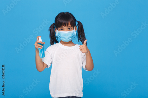 Cute Asian girl wearing a mask and washing her hands with alcohol to prevent spreading the disease on a white background. Prevention of the spread of influenza virus Coronary COVID-19 influenza