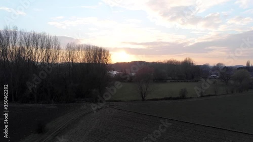 Aerial droneshot of open isolated agricultural land surrounded by trees while sun goes down in winter blue clouds. Vertical pan. Drone lands in the grass. photo