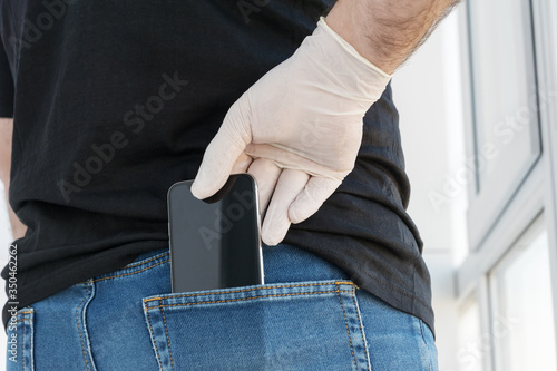  man's hand in white medical glove takes out black smartphone from back pocket of his jeans, protection measures from bacteria, viruses, coronavirus, healthcare concept, new communication format