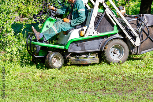 An off-road tractor mower is a necessary garden tool for maintaining park lawns near large shrubs and trees.