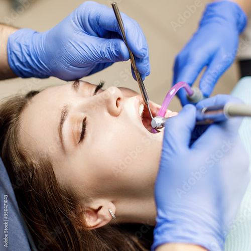 Dentist treating teeth to young woman patient in clinic.