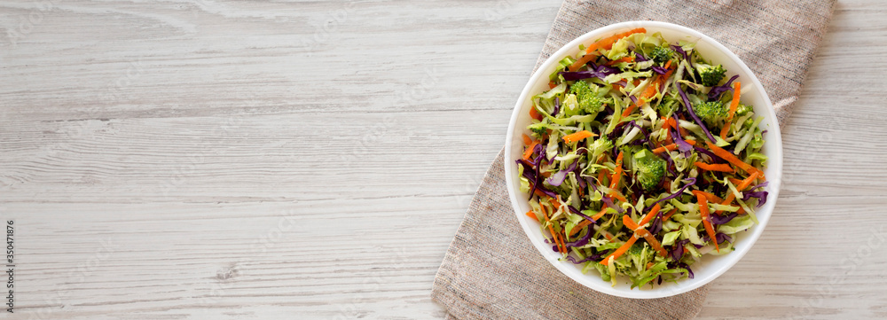 Homemade Raw Shredded Broccoli Slaw in a white bowl on a white wooden background, top view. Overhead, from above, flat lay. Space for text. Homemade Raw Shredded Broccoli Slaw in a white bowl on a white wooden background, top view. Overhead, from above, flat lay. Space for text.