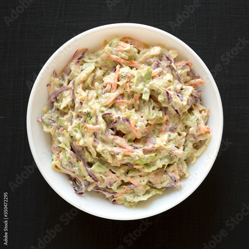 Homemade Creamy Broccoli Slaw in a white bowl on a black surface, top view. Flat lay, from above, overhead.