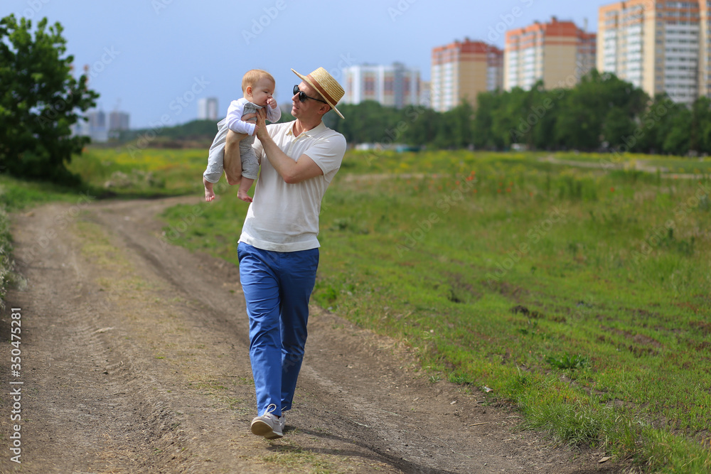 dad with a baby of eight months have fun playing in the grass in the sun in the park on the background of houses