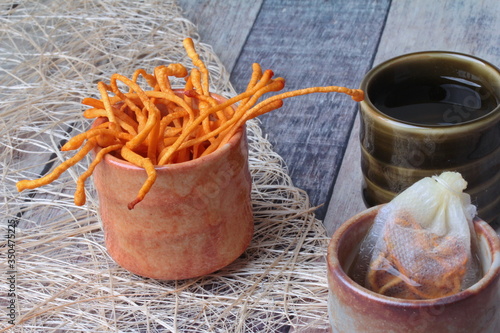 Golden cordyceps mushroom in cup ,herbal tea bag of  golden cordyceps militaris and a cup of tea served on wood