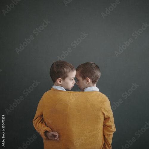 Rear view of twin boys wrapped in jacket standing indoors