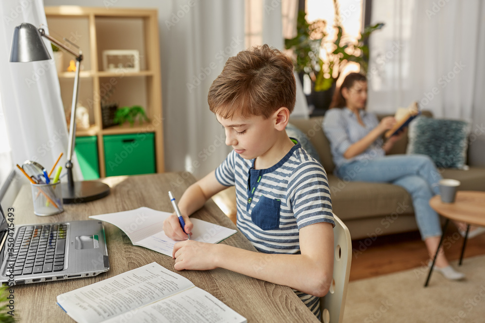 Fototapeta premium children, education and learning concept - happy student boy with book writing to notebook at home